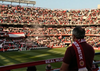 Aficionados del Real Murcia llenando el Estadio Enrique Roca con bufandas grana y blancas bajo la luz dorada de la tarde