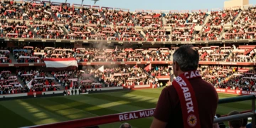 Aficionados del Real Murcia llenando el Estadio Enrique Roca con bufandas grana y blancas bajo la luz dorada de la tarde