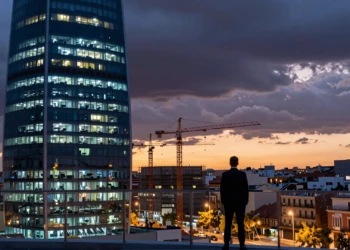 Ejecutivo frente al skyline de Madrid al atardecer con un centro de datos moderno y grúas bajo nubes de tormenta