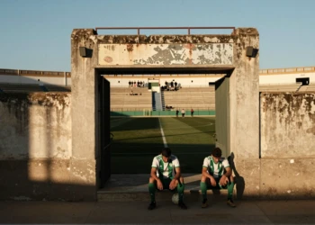 Jugador del Córdoba CF sentado en las gradas de un estadio andaluz al atardecer, con jersey blanco y verde