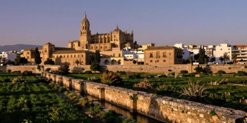 Catedral de Murcia al atardecer junto al Río Segura con acequias árabes medievales y huerta verde en primer plano