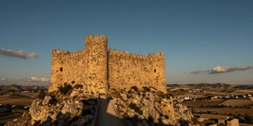 Castillo medieval de piedra dorada en lo alto de una colina árida de Murcia bajo un cielo azul cobalto al atardecer