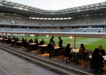 Interior del estadio del Real Murcia en un día sin partido, con terrazas de café animadas y salones VIP iluminados