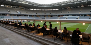 Interior del estadio del Real Murcia en un día sin partido, con terrazas de café animadas y salones VIP iluminados
