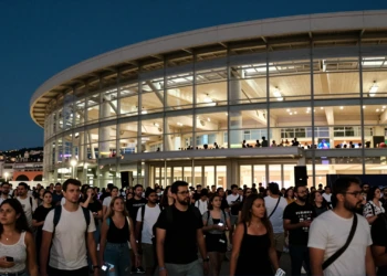 Multitud de asistentes a un concierto frente a un gran pabellón moderno iluminado de noche en una ciudad mediterránea