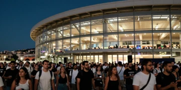 Multitud de asistentes a un concierto frente a un gran pabellón moderno iluminado de noche en una ciudad mediterránea