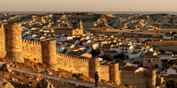 Viajero contemplando paisaje de Murcia al atardecer con castillo medieval, pueblo histórico y costa mediterránea
